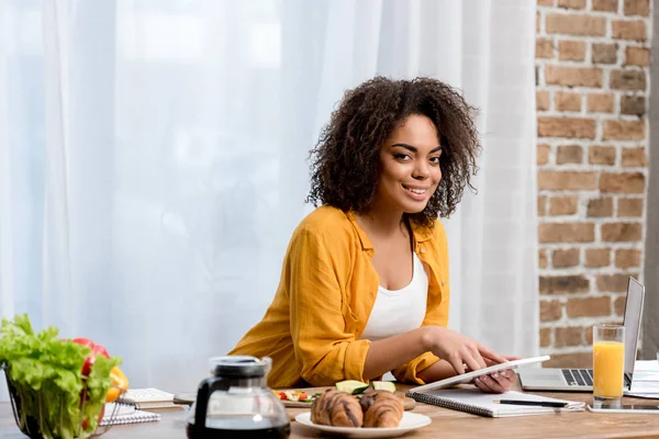 Beautiful young woman working at home with food on table — Stock Photo