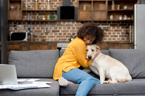 Schöne junge Frau, die zu Hause arbeitet und mit ihrem Hund kuschelt — Stockfoto