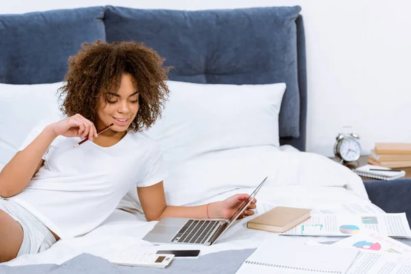 Glückliche junge Frau, die zu Hause mit Laptop im Bett arbeitet — Stockfoto