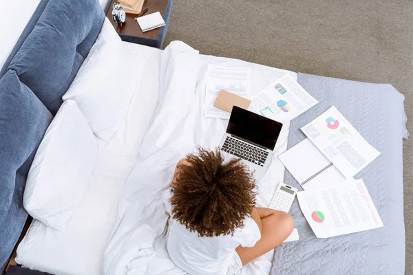 High angle view of young woman working with laptop and documents on bed — Stock Photo