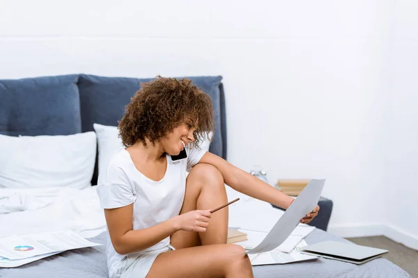 Feliz joven hablando por teléfono y haciendo papeleo en casa - foto de stock