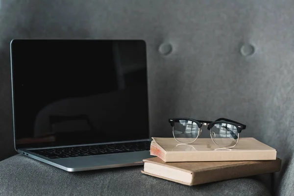 Laptop with empty screen and books lying on grey chair — Stock Photo