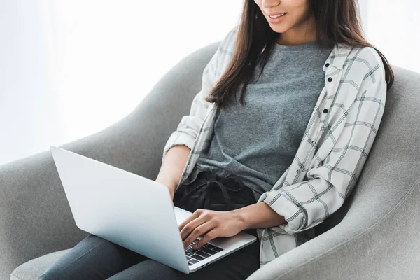 Giovane ragazza seduta sulla sedia e al lavoro sul computer portatile — Foto stock