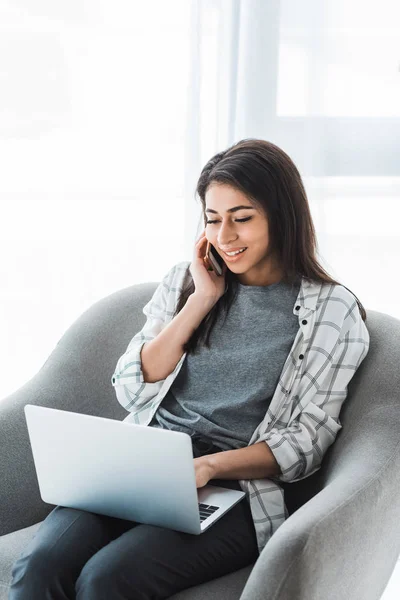 Africano americano mulher sentada na cadeira e falando ao telefone enquanto trabalhava no laptop — Fotografia de Stock