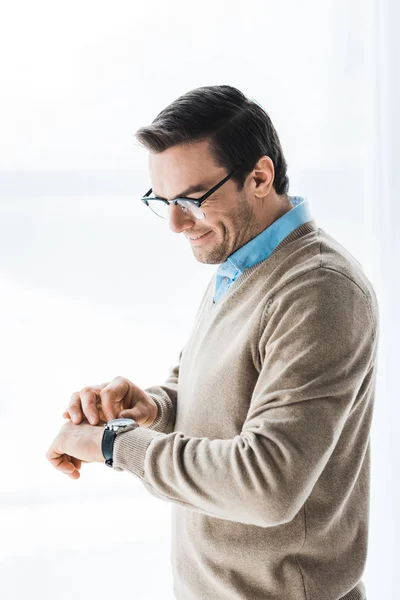 Привлекательный мужчина в очках проверяет часы у окна — стоковое фото