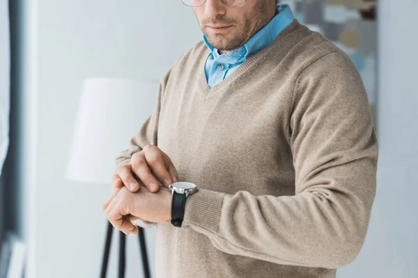 Чоловік в окулярах і повсякденному одязі дивиться на свій годинник — стокове фото