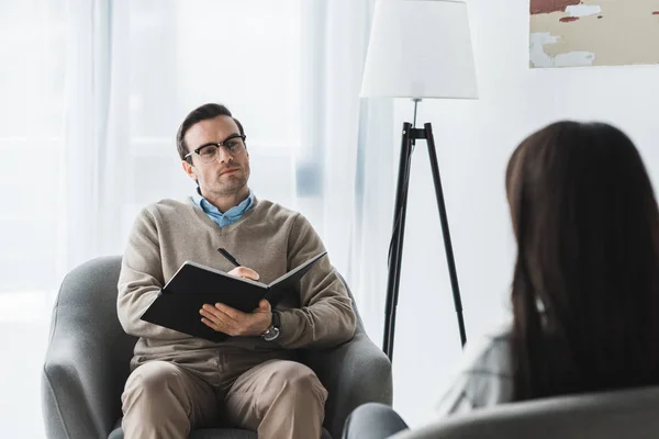 Male therapist in glasses listening to female patient in light office — Stock Photo