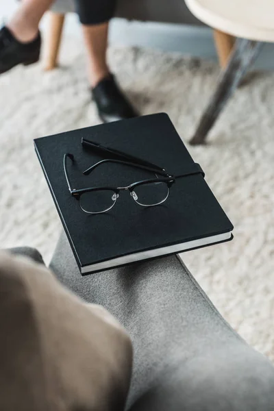 Vista de cerca de las gafas en el cuaderno delante de la mujer en el consultorio médico - foto de stock