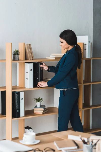 Businesswoman stacking folders on shelf in modern office — Stock Photo