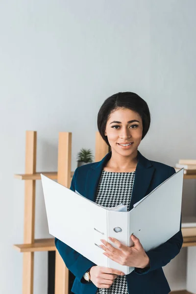 Улыбающаяся деловая женщина держит папку в современном офисе — стоковое фото