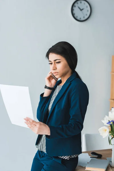 Mujer de negocios mirando el contrato y hablando por teléfono - foto de stock