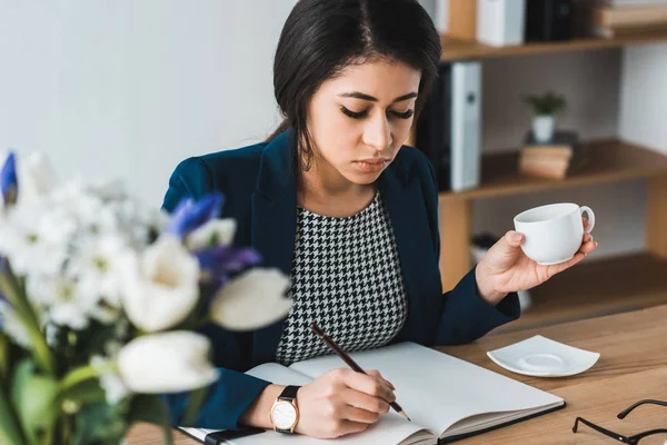 Empresaria trabajando por mesa con taza de café en la mano - foto de stock