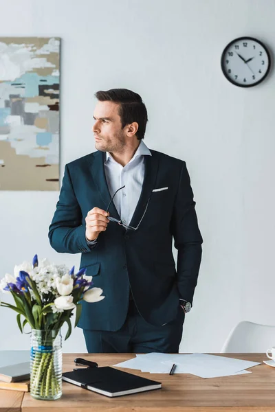 Serious businessman holding glasses in his hand and looking away — Stock Photo