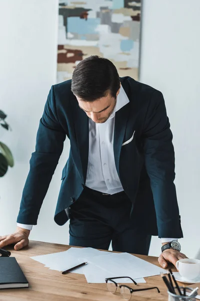 Nachdenklicher Geschäftsmann stützt sich mit Geschäftspapieren auf den Tisch — Stockfoto