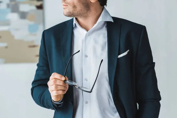 Empresario vistiendo traje y sosteniendo gafas en su mano - foto de stock