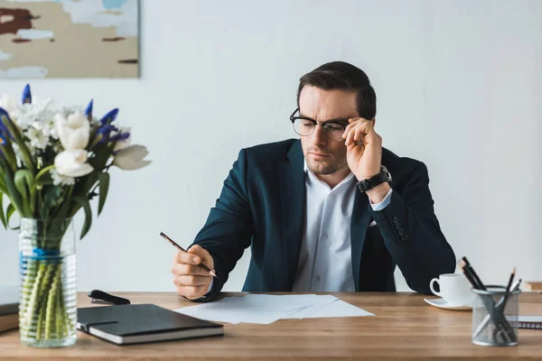 Geschäftsmann mit Brille schaut im Büro auf Vertragspapiere auf dem Tisch — Stockfoto