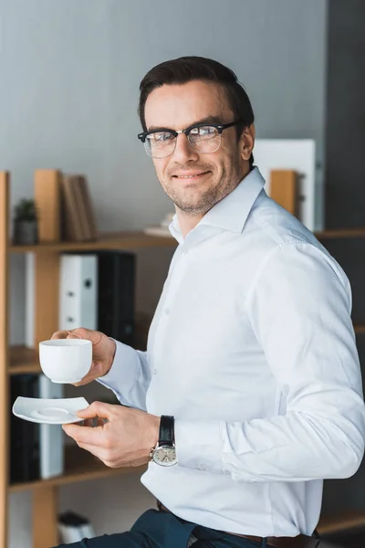 Улыбающийся мужчина-менеджер наслаждается кофе во время перерыва в современном офисе — стоковое фото