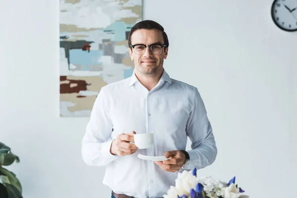 Усміхаючись чоловічого менеджер в окулярах, тримаючись за чашку кави сучасні офісні — стокове фото