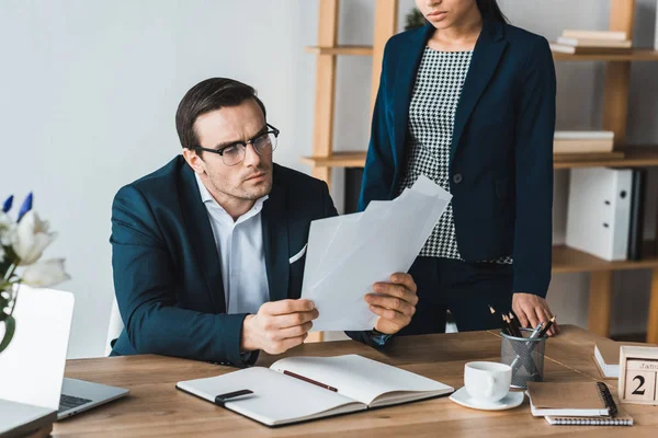 Compañeros de negocios mirando los papeles de contrato por mesa en la oficina - foto de stock