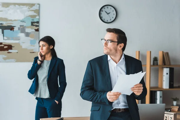 Businessman holding contract while businesswoman talking on phone in modern office — Stock Photo