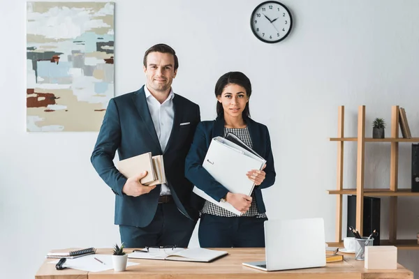 Empresario y mujer de negocios sosteniendo carpetas por mesa de trabajo - foto de stock