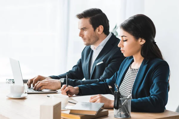 Business colleagues working by table with laptop in modern office — Stock Photo