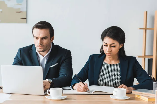 Homme d'affaires et femme d'affaires travaillant par table avec ordinateur portable dans le bureau léger — Photo de stock