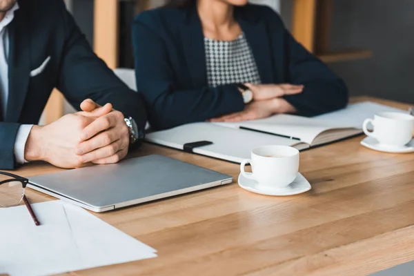 Business colleagues working by table with coffee cups in light office — Stock Photo