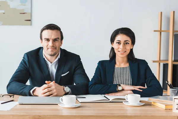Lächelnder Geschäftsmann und Geschäftsfrau am Tisch mit Kaffeetassen im hellen Büro — Stockfoto