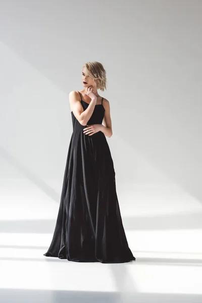 Блондинка молода жінка позує в елегантній чорній сукні, на сірому — стокове фото