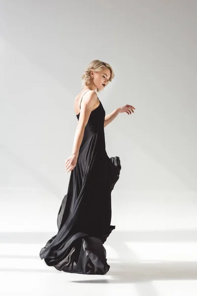 Стильна дівчина позує в елегантній чорній сукні для модної стрільби, на сірому — стокове фото