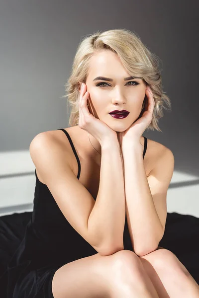 Élégante fille blonde avec maquillage posant en robe noire, sur gris — Photo de stock