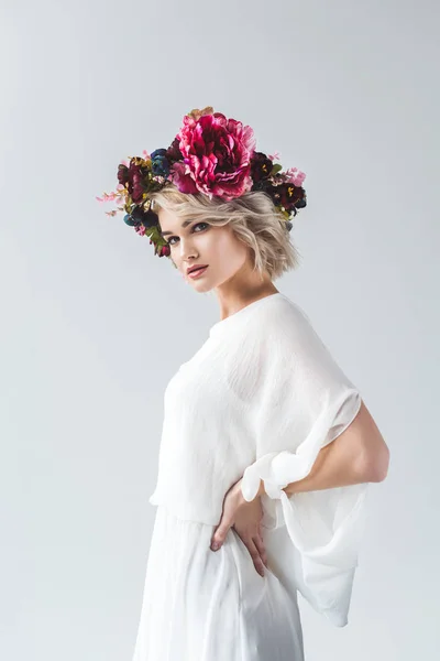 Приваблива блондинка позує в білій сукні і квітковому вінку, ізольована на сірому — стокове фото