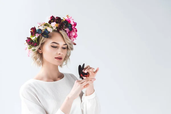 Beautiful tender young woman posing in floral wreath with butterfly on hands, isolated on grey — Stock Photo