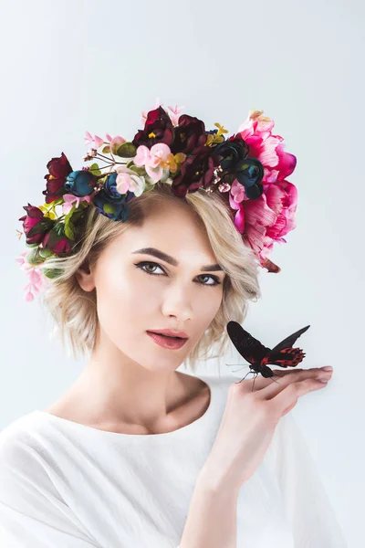 Atractiva chica posando en corona de flores con hermosa mariposa en la mano, aislado en gris - foto de stock