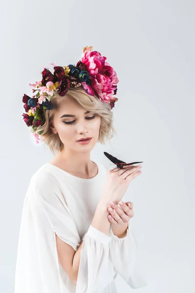 Jolie femme posant en couronne de fleurs avec papillon sur les mains, isolé sur gris — Photo de stock