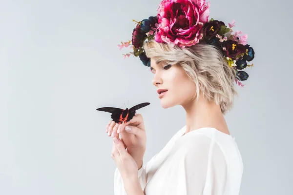 Beautiful girl posing in floral wreath with alive butterfly on hands, isolated on grey — Stock Photo
