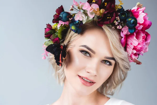 Attractive tender girl posing in wreath with beautiful butterfly on cheek, isolated on grey — Stock Photo