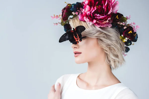 Menina elegante posando em coroa floral com bela borboleta viva no rosto, isolado em cinza — Fotografia de Stock