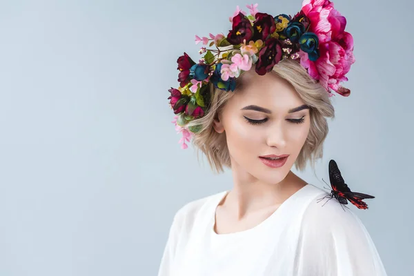 Modelo bonito posando em coroa floral com borboleta no ombro, isolado em cinza — Fotografia de Stock