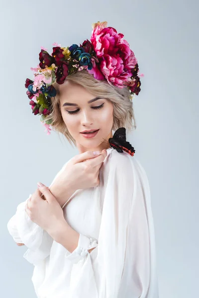 Attractive model posing in floral wreath with butterfly on shoulder, isolated on grey — Stock Photo