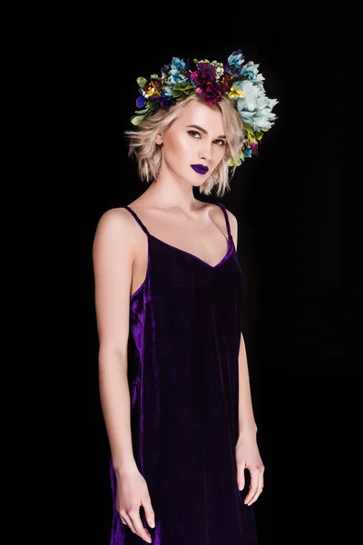 Красива блондинка позує в фіолетовій сукні і квітковому вінку, ізольована на чорному — стокове фото