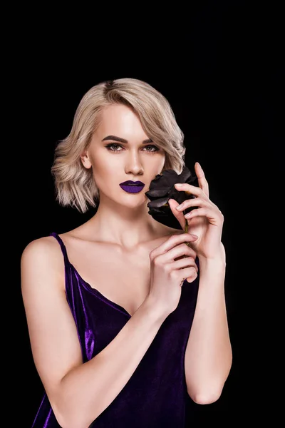 Blonde girl posing in fashionable purple dress with black rose, isolated on black — Stock Photo