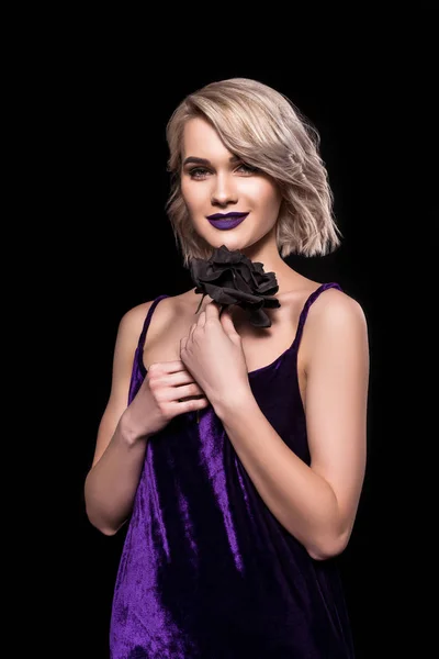 Heureuse fille blonde posant en robe violette avec rose noire, isolé sur noir — Photo de stock
