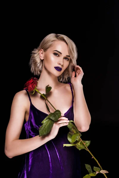 Schönes Mädchen posiert in lila Kleid mit roter Rose, isoliert auf schwarz — Stockfoto