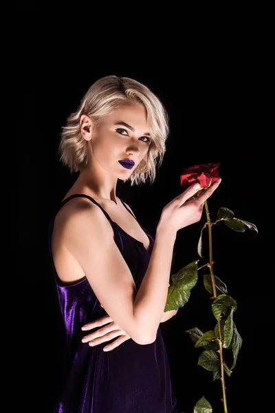 Menina loira atraente posando em vestido roxo com flor de rosa vermelha, isolado em preto — Fotografia de Stock