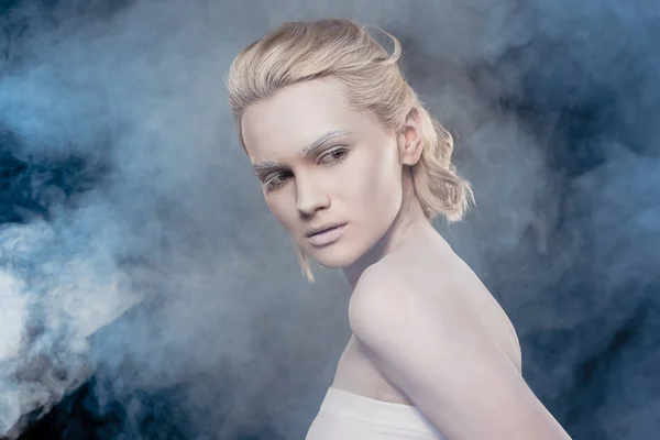 Beautiful blonde girl with white makeup posing for fashion shoot in smoky studio — Stock Photo