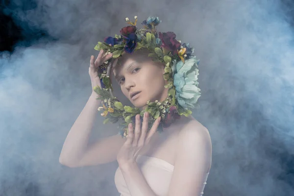 Attraktives zartes Mädchen mit weißem Make-up mit Blumenkranz im rauchigen Studio — Stockfoto