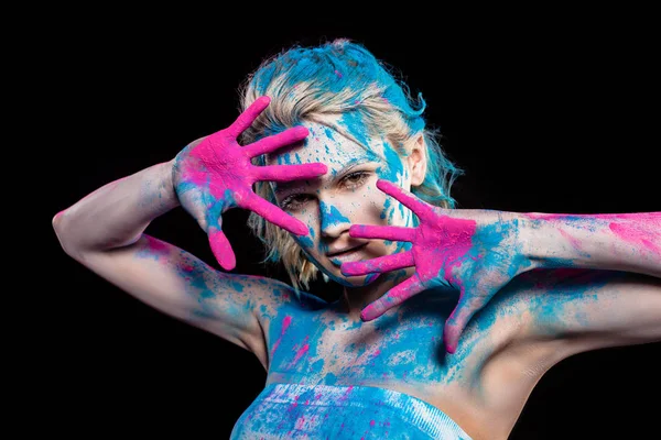 Menina atraente gesto e posando em pó holi rosa e azul, isolado em preto — Fotografia de Stock