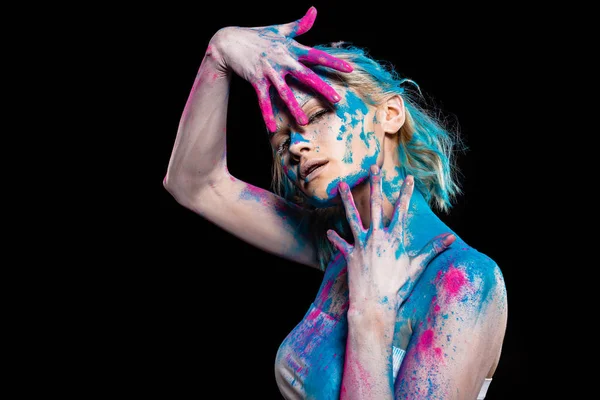 Mulher atraente posando em tinta holi rosa e azul, isolado em preto — Fotografia de Stock